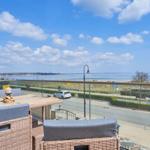 Terrasse mit Sitzgelegenheiten und Blick auf Wasser und Strandpromenade.