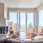 Wohnzimmer mit Kamin, Fernseher und Meerblick durch große Fenster.