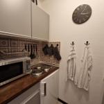Küche mit Mikrowelle, Herd, Kühlschrank und Wanduhr.