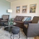 Wohnzimmer mit Sofa, zwei Sesseln und runden Tischen auf Teppich.