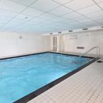 Innere Schwimmhalle mit blauem Wasser, weißen Wänden und Bodenfliesen sowie einer Treppe.