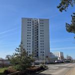 Hochhaus mit vielen Fenstern, Straße mit Bäumen und klarem Himmel.