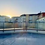 Terrasse mit Blick auf städtische Gebäude bei Sonnenuntergang. Bodenfliesen und Metallgeländer.