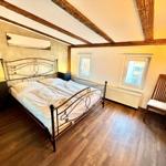Schlafzimmer mit Doppelbett, Holzboden und Holzbalkendecke. Zwei Fenster und Stuhl.