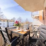 Terrasse mit Tisch, Stühlen und Blumen. Blick auf Wohnhäuser und Bäume.