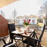 Balkon mit Tisch, Stühlen und Blumen. Blick auf Wohnhäuser und Bäume.