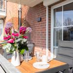 Terrasse mit Tisch, Stühlen und Blumenarrangement vor Backsteinmauer und Fenster.