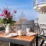 Terrasse mit Tisch, Stühlen und Blumenarrangement. Blick auf Wohngebiet und Himmel.