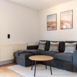 Ein Wohnzimmer mit grauem Sofa, runder Tisch und zwei Wandbildern.