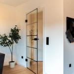 Wohnbereich mit Glaswand, Pflanze und Sofa. Küchenbereich mit Holzoberfläche.