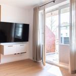 Wohnzimmer mit Fernseher, Holzboden und Balkontür.