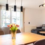 Essbereich mit Tisch, Stühlen und Blumen. Wohnbereich mit Sofa und Wandbildern.