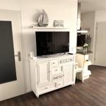 Living room with TV cabinet, door, and kitchen area in background.