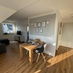 Wohn- und Essbereich mit Holzboden, Esstisch und Sofa. Wand mit Bildern und Fenster.