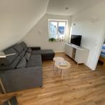 Wohnzimmer mit Sofa, Fernseher und Holzboden. Schlafzimmer mit Bett sichtbar.