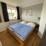 Schlafzimmer mit Holzbett, blauer Bettdecke und Fenster mit Blick.