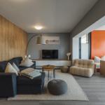 Wohnzimmer mit Sofa, Sessel und Esstisch. Holzwand und orange Wand.