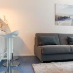 Ein Wohnbereich mit grauem Sofa, Barhocker und Wandbild.