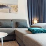 Ein grauer Ecksofa mit Kissen und einer Decke vor einem Fenster mit Vorhängen.