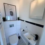 Badezimmer mit Toilette, Waschbecken und Spiegel. Wand mit schwarzem Streifen und Mosaikboden.