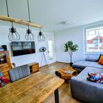 Wohn- und Essbereich mit Sofa, Tisch und Fernseher. Holzfußboden und große Fenster.