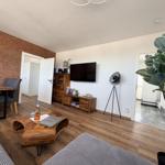 Wohnzimmer mit Holzboden, Fernseher, Couch und Essbereich mit Backsteinwand.