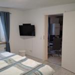 Schlafzimmer mit Bett, TV und Fenster. Tür führt in die Küche.