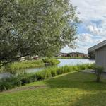 Green lawn in front of a house with a view of a lake and trees.