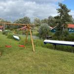 Behind the house is a playground with swings and climbing frame. Two canoes are on the lawn.