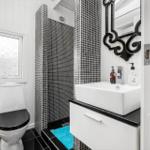 Badezimmer mit Toilette, Waschbecken und Dusche mit schwarz-weißen Fliesen.