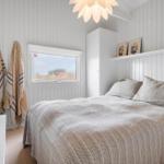 Schlafzimmer mit Bett, Fenster und Wandregal. Weiße Holzwandverkleidung und Deckenleuchte.