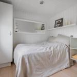 Schlafzimmer mit weißem Bett, Kleiderschrank und Regal. Wandverkleidung und Holzboden.