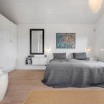 Schlafzimmer mit Bett, Wandspiegel und Fenster. Holzboden und weiße Wände.
