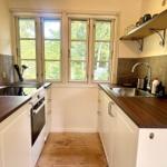 Kitchen with white cabinets, wooden countertops, and windows to the garden.