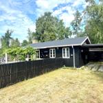 Black wooden house with white window frames and garden fence. Surrounded by trees and grass.