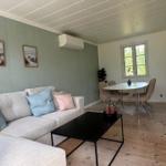 Living and dining area with sofa, table, and chairs. Wooden floor and wall pictures visible.
