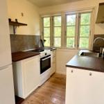 Kitchen with white cabinets, dark countertop, and wooden floor. Windows with view of greenery.