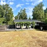 House with terrace, grill and garden. Surrounded by trees under blue sky.