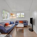 Living room with blue sofas, wooden table, and TV. White walls and two windows.