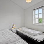 Two beds with white bedding, nightstand, and window with view of greenery.