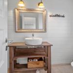 Bathroom with sink, mirror, and toilet. Wooden vanity with toilet paper box.
