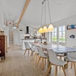 Dining area with long table and chairs. Kitchen and living area in the background.