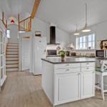 Kitchen with island, white cabinets, and hardwood floors. Background: stairs and white cabinet.