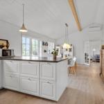 Kitchen with island, white cabinets, and wood floor. Dining area with chairs and windows.