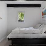 Schlafzimmer mit Bett, Nachttisch und Fenster. Deckenbalken und Wandbild sichtbar.
