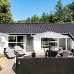 Terrasse mit Liegen, Tisch und Sonnenschirmen. Haus mit dunklem Dach und weißen Wänden.