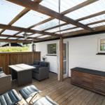 Terrasse mit Sitzgelegenheiten unter einer Holzkonstruktion mit Glasdach.