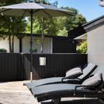Terrasse mit zwei Liegen, Sonnenschirm und weißer Backsteinwand.