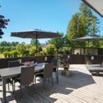 Terrasse mit Tisch, Stühlen, Sonnenschirmen und Liegen. Holzdecke und grüne Umgebung.