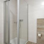 Dusche mit Glaswand, Toilette und WC-Beschlag an Holzpaneelwand.
